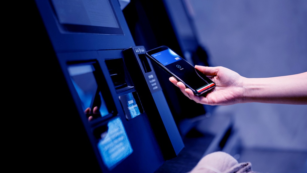 Close up of a young Asian woman using contactless payment via smartphone to pay for her shopping at self-checkout kiosk in a store