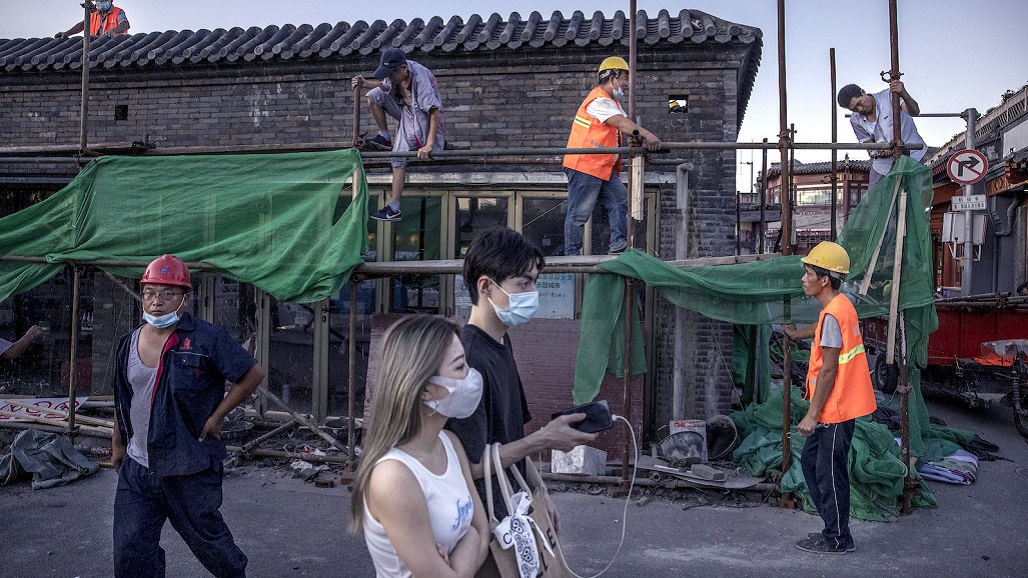BEIJING, CHINA - AUGUST 24: People walk by construction workers as they work on a traditional style building in a shopping district in the Houhai Lake area on August 24, 2021 in Beijing, China. While cases still remain relatively low compared to many countries, China is containing its most recent COVID-19 outbreak after workers in the arrivals area at Nanjing International Airport were infected with the highly contagious Delta variant and it spread to dozens of cities in at least 18 provinces. (Photo by Kevin Frayer/Getty Images)