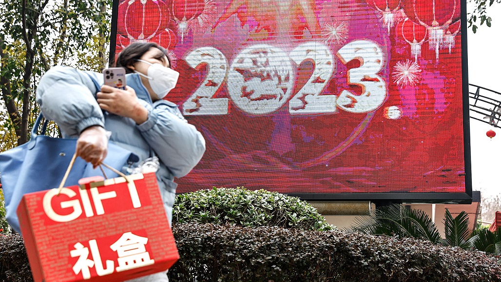 WUHAN, CHINA - DECEMBER 31: People wearing face masks walk past a screen displaying the year 2023 along a street on December 31, 2022 in Wuhan, China. (Photo by Getty Images)